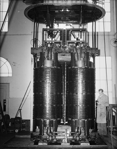 Man standing beside two large cylindrical transformers.
