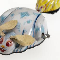 Wind-up metal white & blue rabbit. Red-brown eyes, yellow nose, floppy cream ears. Small yellow rabbit behind.