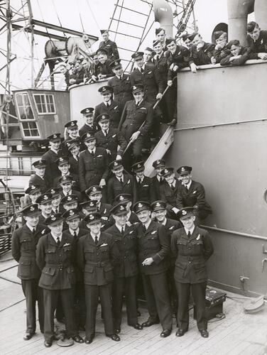 Officers and men plus two sailors, all in uniform, pose onboard a ship.