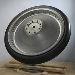 Large silver metal wheel with black rubber tyre. The wheel hub is convex in shape.