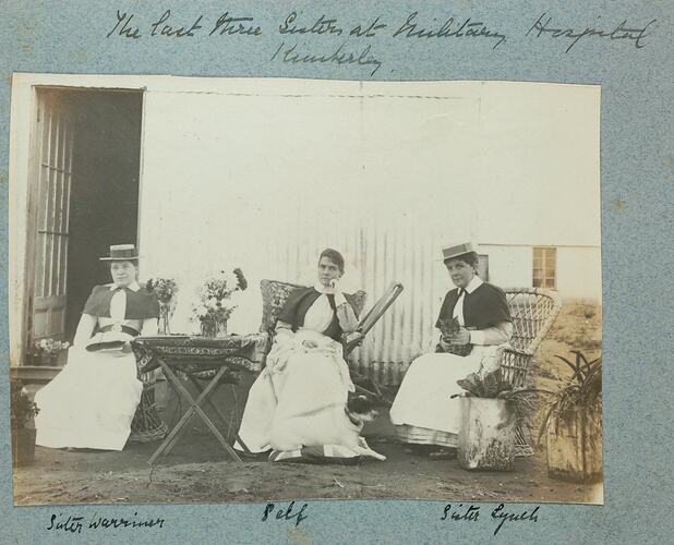 Three woman in nurses uniforms sitting in chairs in front of building.