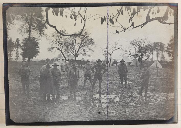 Nine soldiers standing in a muddy field with tents.