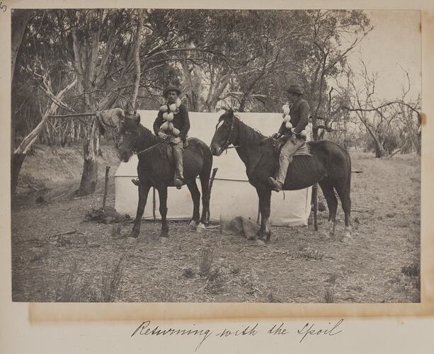 Two men on horseback at their camp. Each man carries strings of emu eggs across his shoulders. Tent behind them.