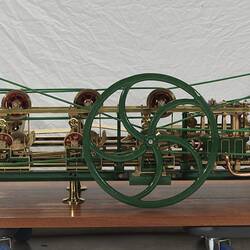 Paper making machine miniature model made of metal. Detail of larger green wheel. Wooden base.