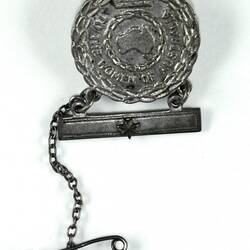 Front of circular badge with bar and pin below.