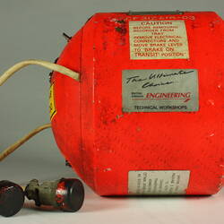 Red cylindrical container with two electrical cords at one end.