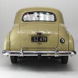 Cream holden car, rear view of number plate and polished chrome bumper.