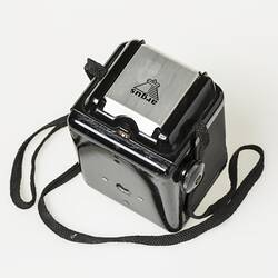 Black plastic box camera, black shoulder strap. Metal pop up viewfinder hood on top.