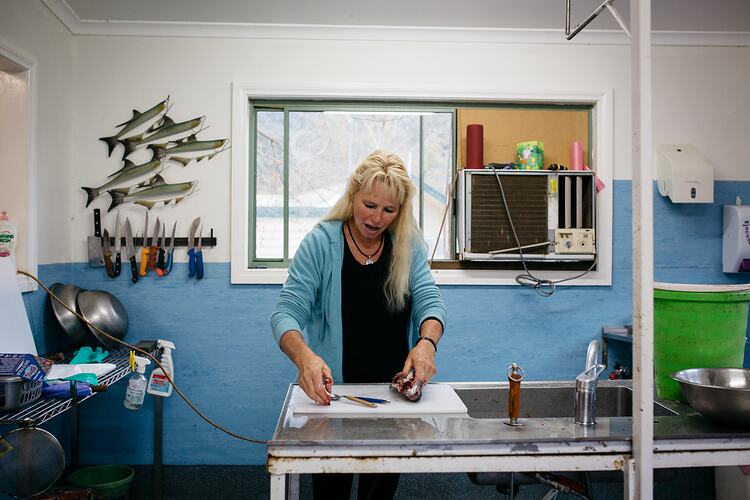 Woman filletting a fish indoors, on steel workbench