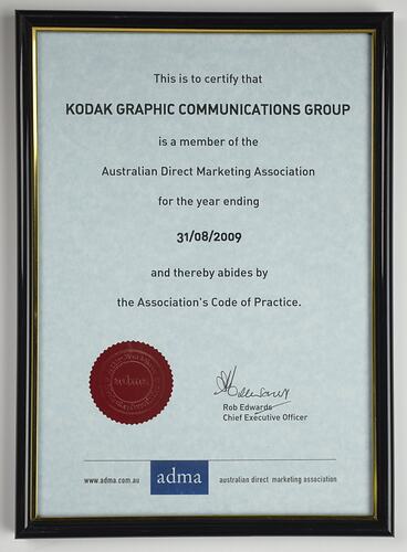 Certificate with red seal in black plastic frame.