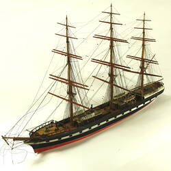 Three quarter view of three masted ship with red hull.
