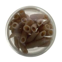 Top view of clear glass jar containing brown tubes of pasta.