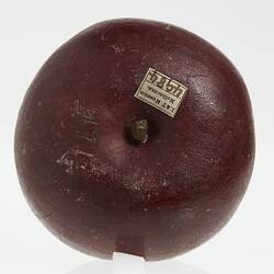 Wax apple model painted dark red. Top view shows short stem and affixed paper label.