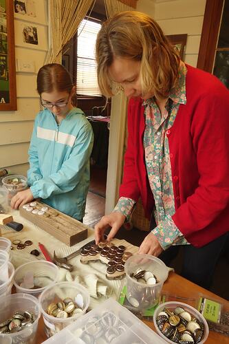 Girl and woman working with bottle tops and other lagerphone components.