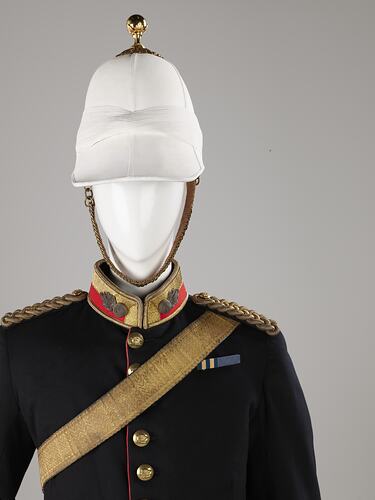 Detail of navy officer's jacket with gold sash, epaulettes. Brass buttons. Red and gold collar, white helmet.