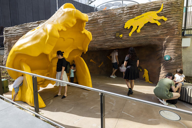 People exploring an outdoor exhibition space, with a large yellow skull in the foreground.