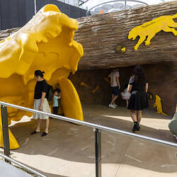 People exploring an outdoor exhibition space, with a large yellow skull in the foreground.