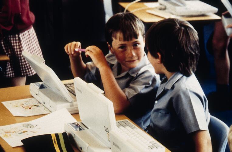 Two young boys in school uniform with laptops.