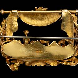 Back of rectangular gold brooch. Ornate detail, open centre. Miner, tools and foliage.