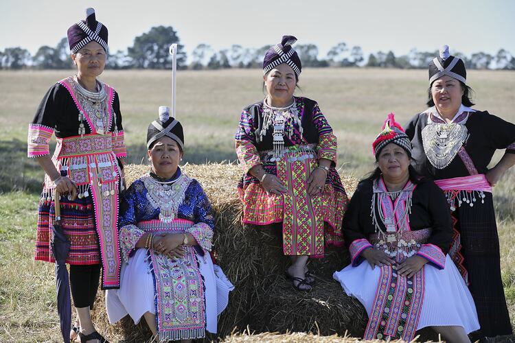 Five women wearing traditional Hmong clothing. Outdoor setting.