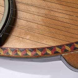 Detail of a timber stringed instrument. Pale wood with black laquered timber detail. Multi stringed.