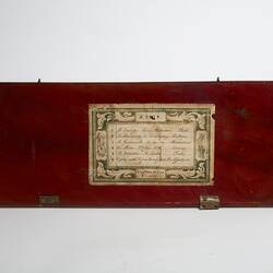 Wooden rectangular lid of box. Decorative paper label affixed.