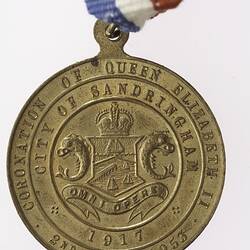Round medal with coat of arms and text surrounding, with red, white and blue ribbon attached.