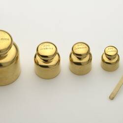 Set of five shiny standard metric gilt brass weights with ivory lifter.