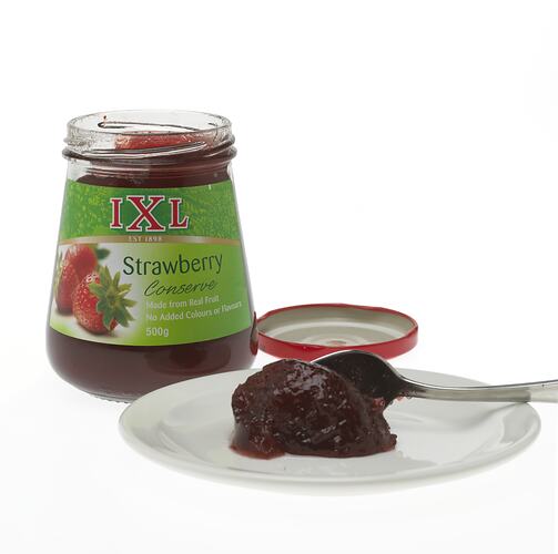 A jar of Strawberry jam and a plate with jam on it.