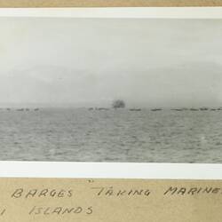 Multiple barges and two ships in open water in the background.