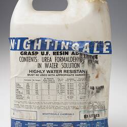 White dirty plastic bottle, white tape instead of lid. Damaged white label has blue and black printing.