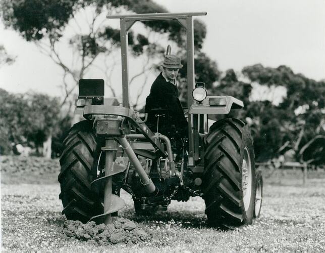 Man looking over the back of a tractor at the hole being made by a Post Hole Digger.