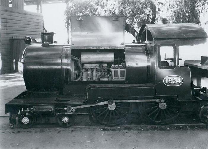 Side view of a scale model of a steam engine, which has cover open to show engine operating it.