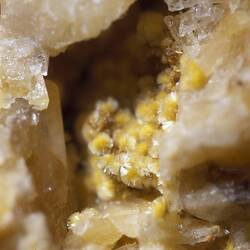 Small sprays of yellow minerals in a cavity surrounded by blocky cream minerals.