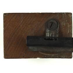 Rectangular brown block of wood, metal clip attached.