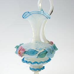 Blue blown-glass ewer, spiral fluted neck, serpentine handle, flattened bulbous body layered with pink, blue, green flowers and leaves.