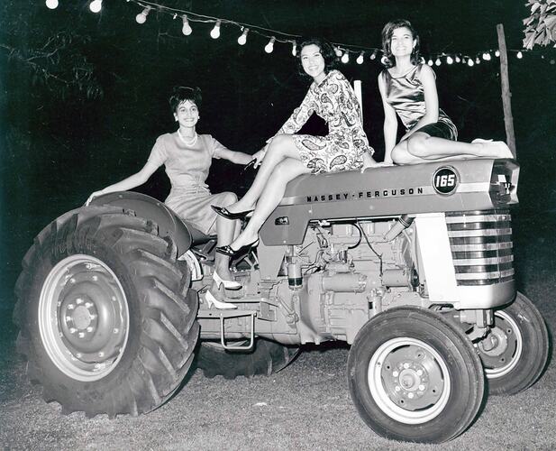 Three female models sit on a tractor