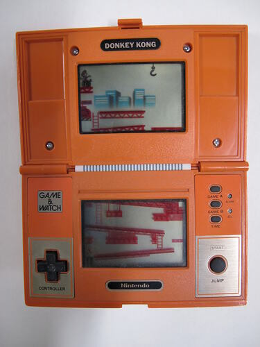 Orange plastic, handheld game console, rectangular, hinged at centre. Screen on top and lower sections.