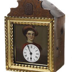 Wooden cuckoo clock with woman's portrait in gold frame. Clock face below her face.