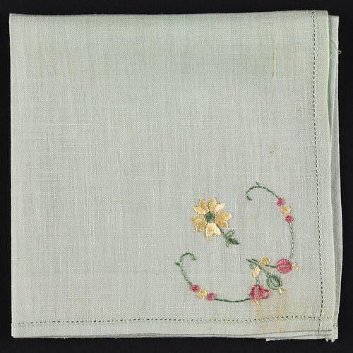 Folded green cotton handkerchief with embroidered flower.
