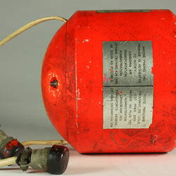 Red cylindrical container with two electrical cords at one end.