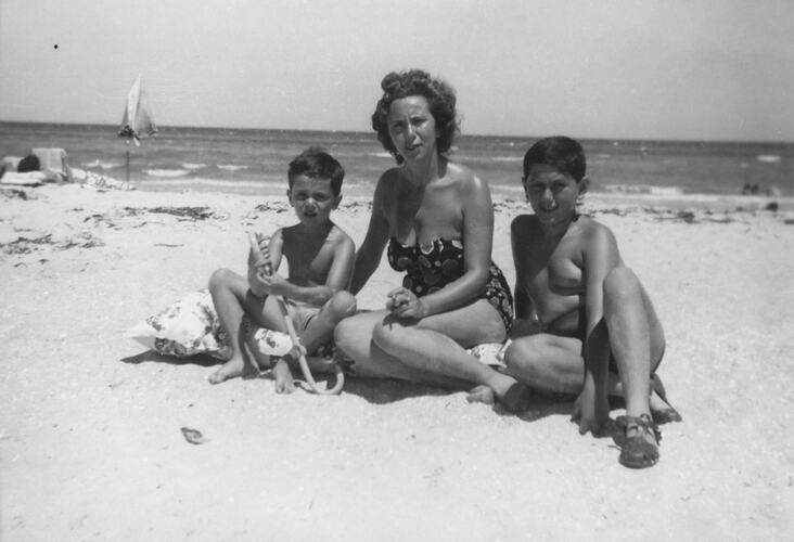 Woman and two boys sitting on a beach.