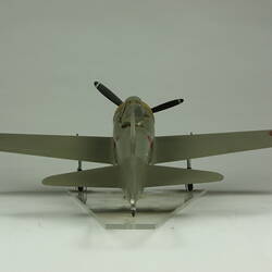 Green grey plane model with red spot on each wing and fusleage. Yellow nose, black propeller. Back view.