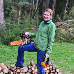Woman standing near a wood pile holding a chainsaw