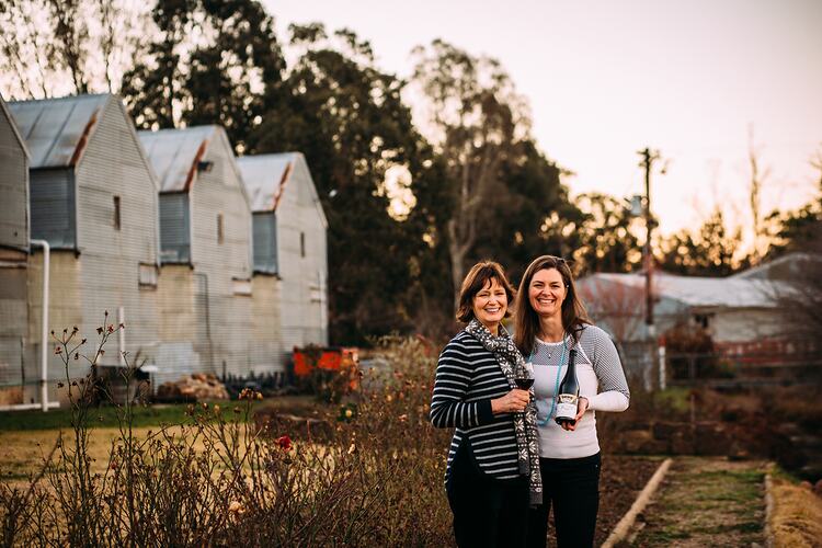 Two women standing near garden bed and sheds.