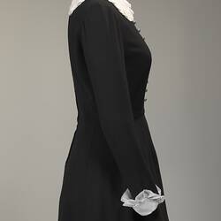 Right side of long sleeved black wool mini dress. White collar and cuffs.