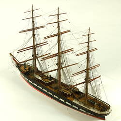Three quarter view of three masted ship with red hull.