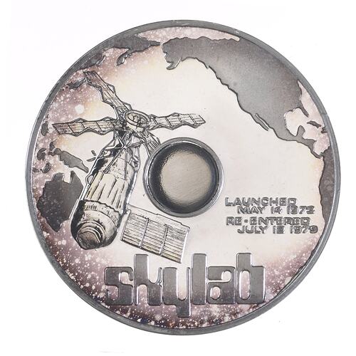 Round silver medal with Skylab depicted in orbit over Eastern Australia. Pacific and North America visible.