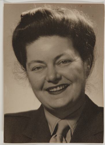 Woman poses and smiles in portrait. Her hair is up in a bun and she wears a dark jacket and lighter shirt and