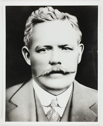 Bust portrait of man with moustache wearing a suit and tie.